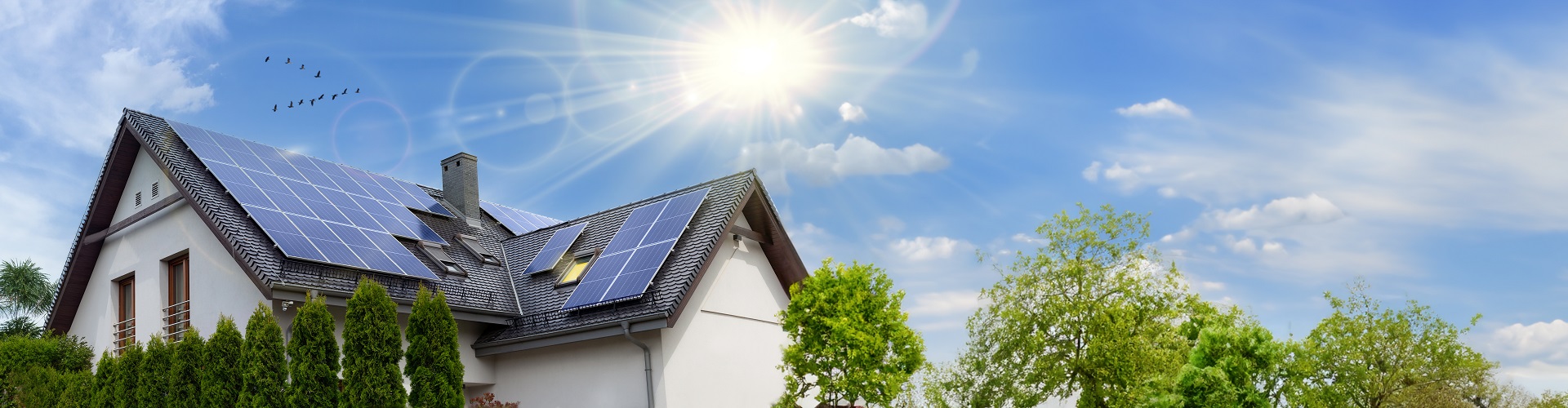 Modernes Einfamilienhaus mit großflächigen Solarpanels auf dem Dach unter strahlendem Sonnenschein und blauem Himmel.
