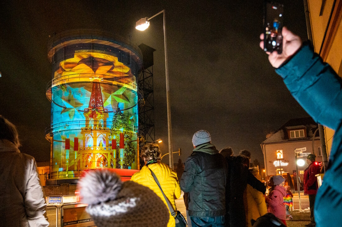 Eine Gruppe von Menschen bestaunt den illuminierten Gaskessel in Bernau.